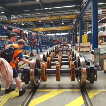 Gruppe besichtigt die Achse mit Rädern eines Zugs in der Wekstatt